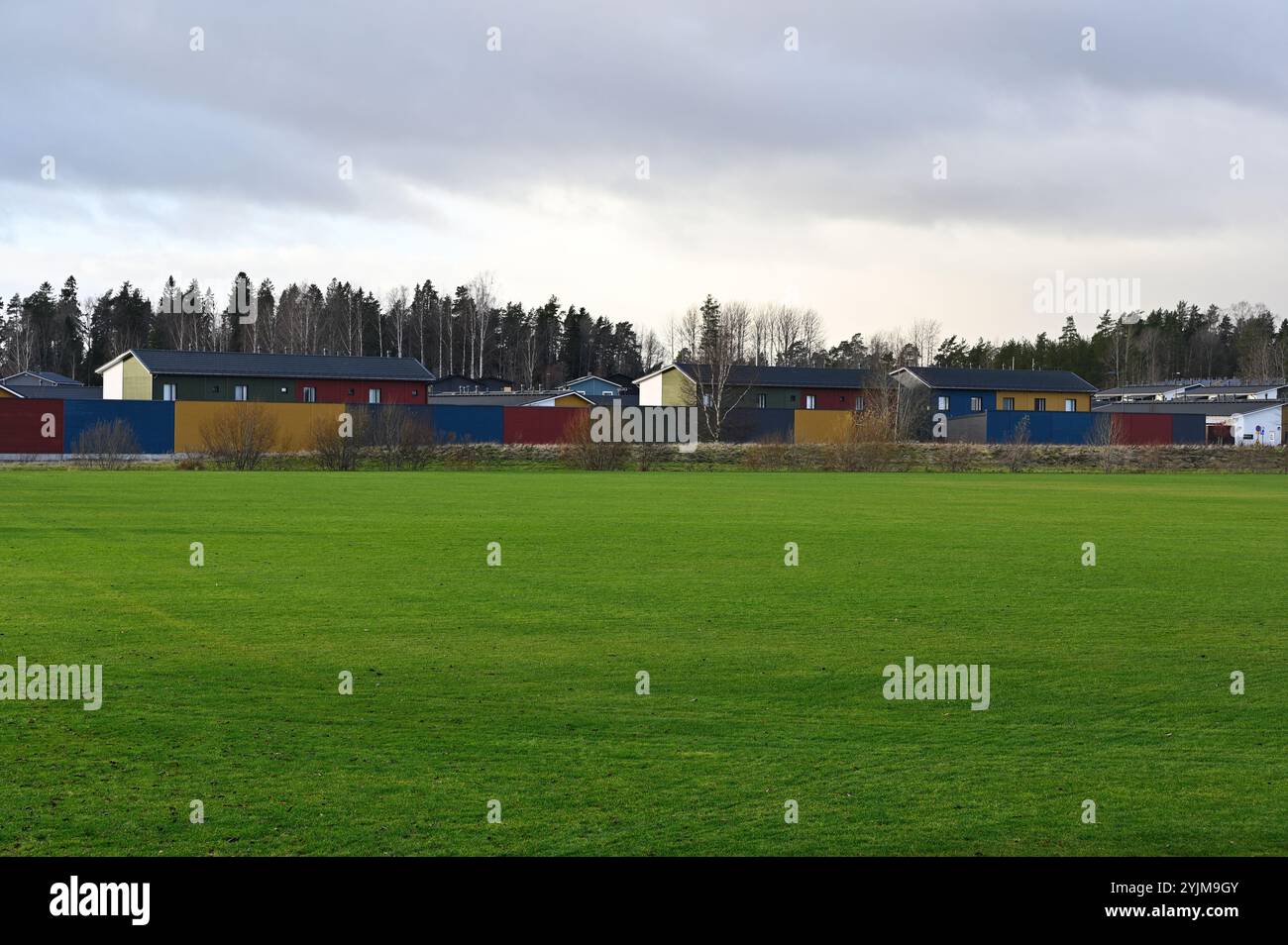 un campo verde con una fila di case moderne sullo sfondo. Le case sono dipinte in vari colori, tra cui rosso, giallo, verde e blu, creatina Foto Stock