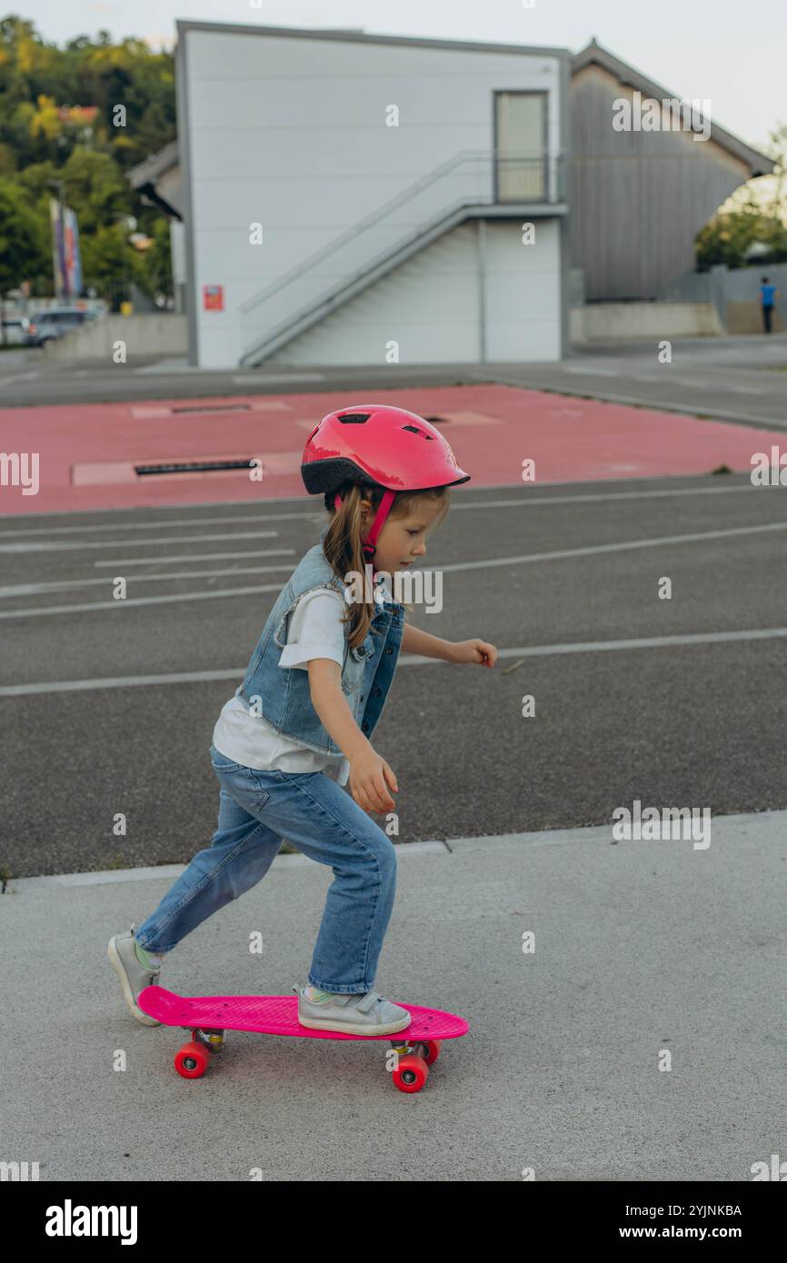 una ragazza carina con un casco rosa cavalca uno skateboard. Foto di alta qualità Foto Stock