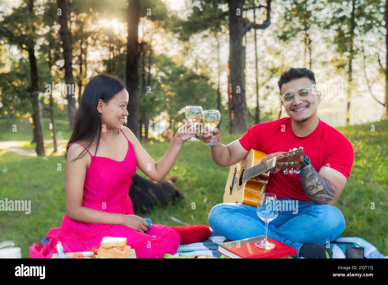 Coppia romantica in un appuntamento nella natura, picnic con cibo suonando la chitarra e godendosi all'aperto sotto il sole Foto Stock