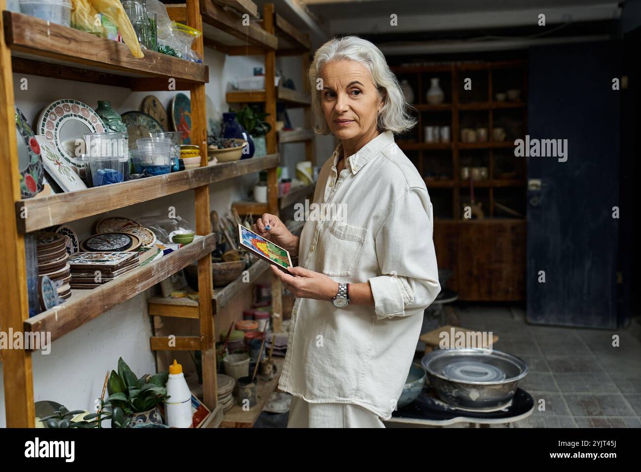 Una bella donna matura cura vivaci ceramiche nel suo ambiente di lavoro accogliente e artistico. Foto Stock