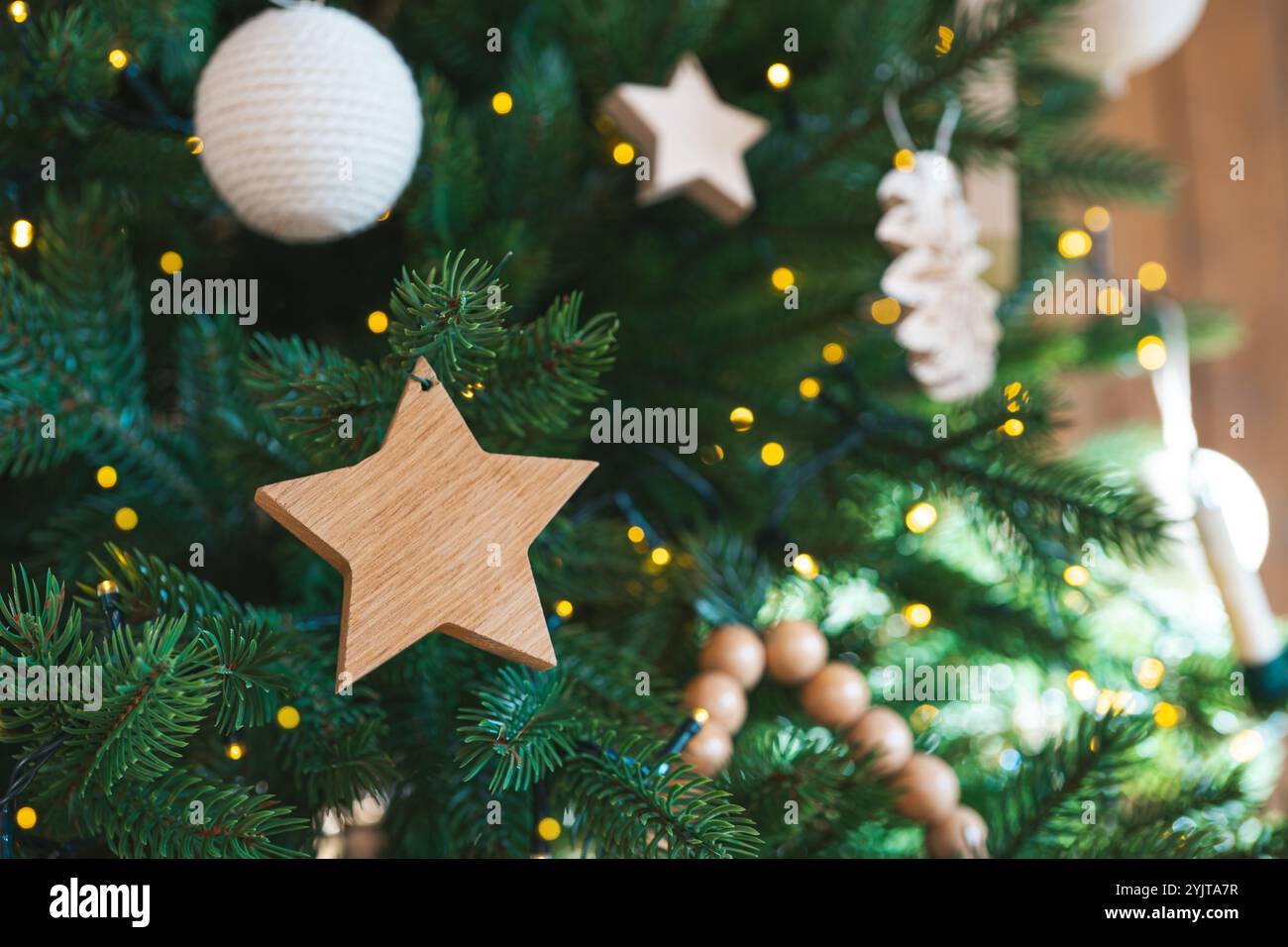 Albero di Natale decorato con ornamenti a stella in legno e palle su sfondo di calde luci. Atmosfera festosa in uno spazio interno per l'inverno Foto Stock