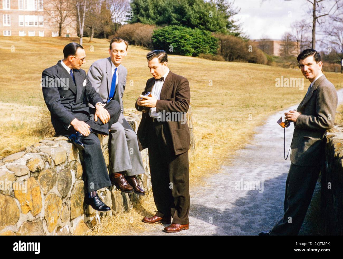 Quattro uomini vestiti in modo intelligente in abiti da lavoro all'aperto, USA c 1953 in piedi seduti a parete Foto Stock