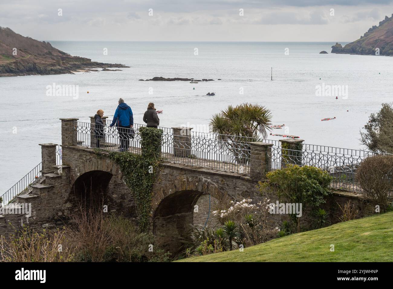 La famiglia si trova su una passerella privata, con ringhiere ornate, sopra Cliff Road e ammira la vista dell'estuario di Salcombe in un grigio giorno di primavera Foto Stock
