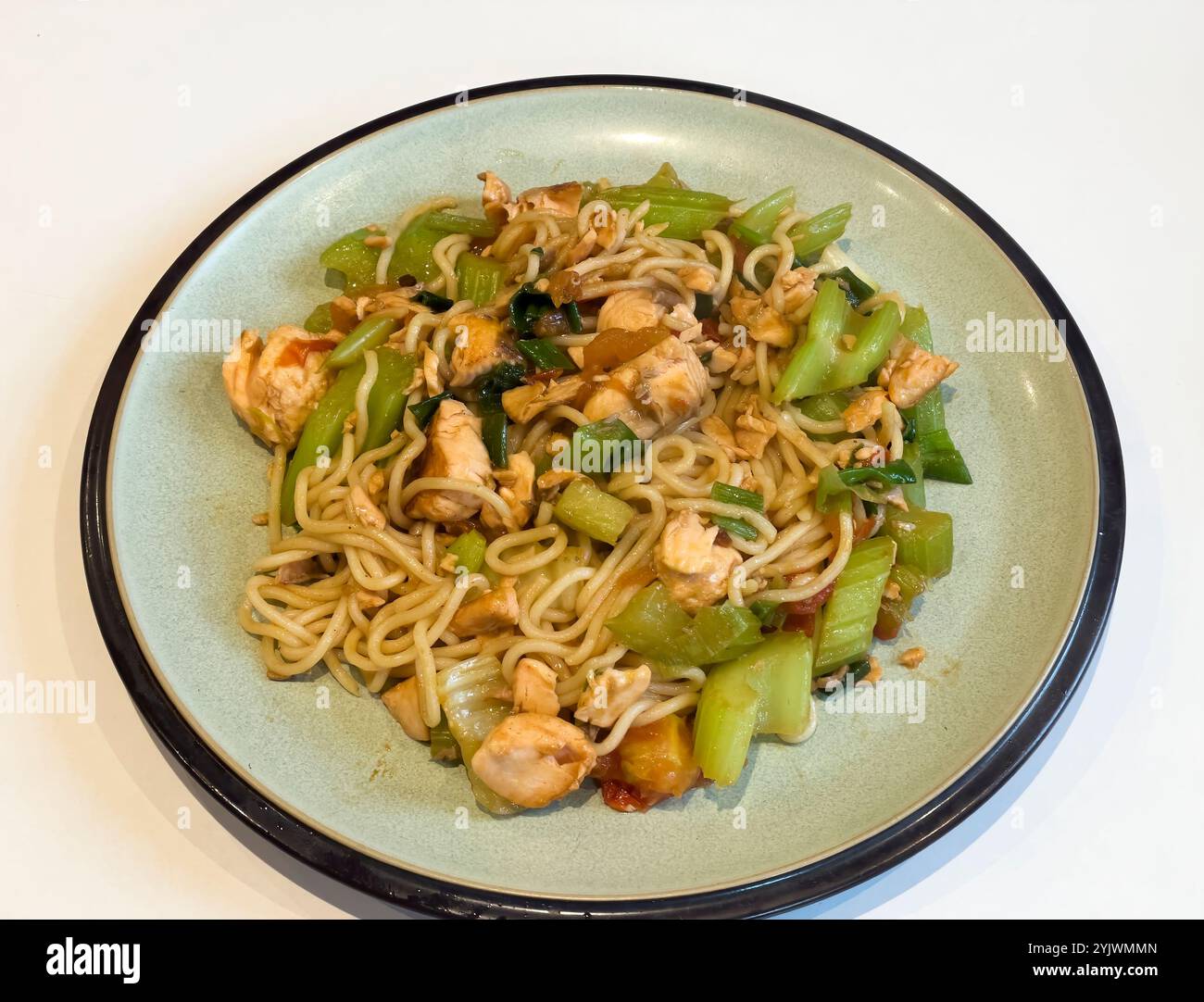 spaghetti saltati in padella con teneri pezzi di salmone e verdure verdi fresche. Perfettamente presentato su un piatto verde chiaro, che mostra un sano e.. Foto Stock