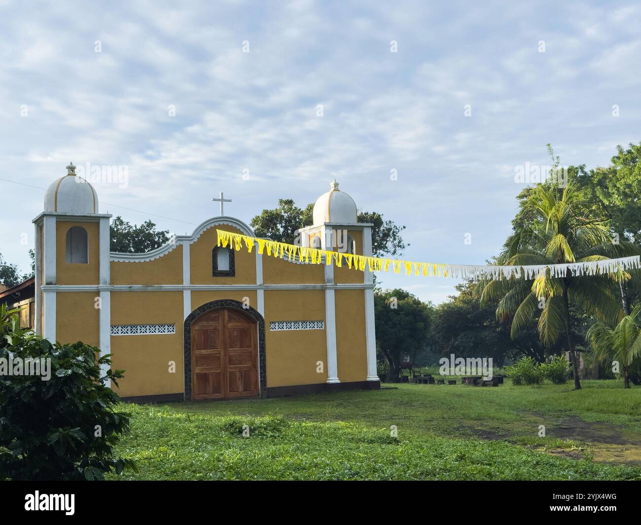 La pittoresca chiesa gialla sorge orgogliosamente tra il verde vivace sotto il cielo azzurro, evocando un'atmosfera tranquilla. Foto Stock
