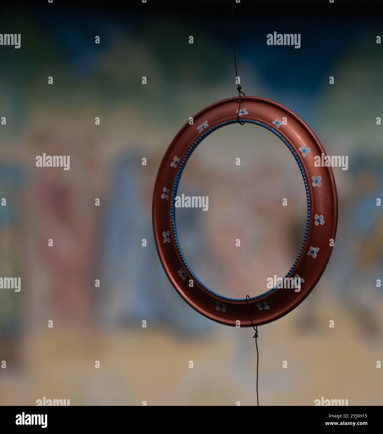 Dipinto a mano di rosso con fiori bianchi e blu, rotondo, telaio vuoto in legno appeso a un filo con sfondo o sfondo color pastello sfocato Foto Stock
