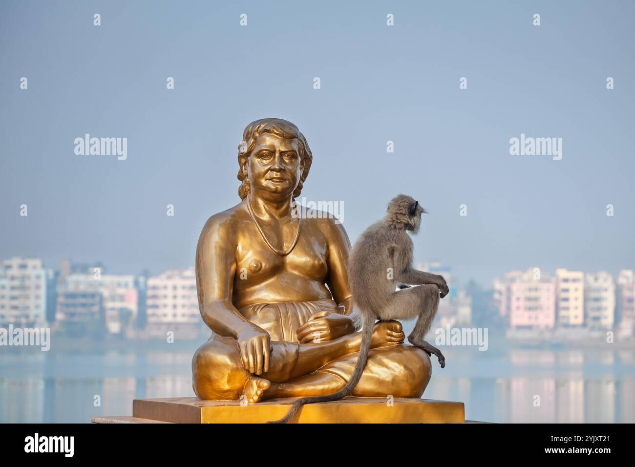 Una scimmia siede accanto a una statua serena, tenendo la mano in un momento cullante che cattura l'interazione tra fauna selvatica e arte, simboleggiando ha Foto Stock