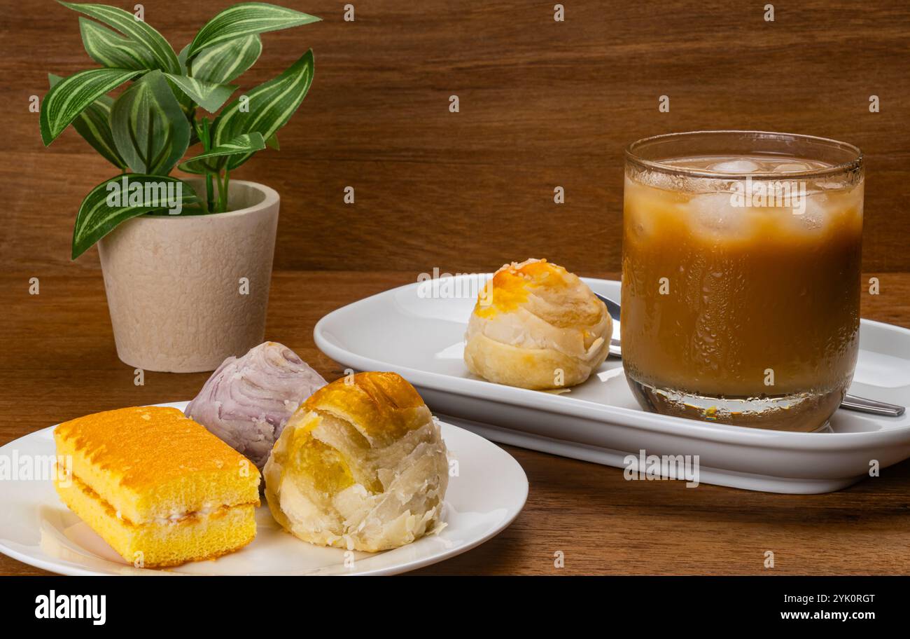 Torta cinese e torta a strati in un piatto di ceramica bianca con una torta cinese che ricopre il sesamo bianco e un bicchiere di caffè a latte freddo con cubetti di ghiaccio su legno Foto Stock