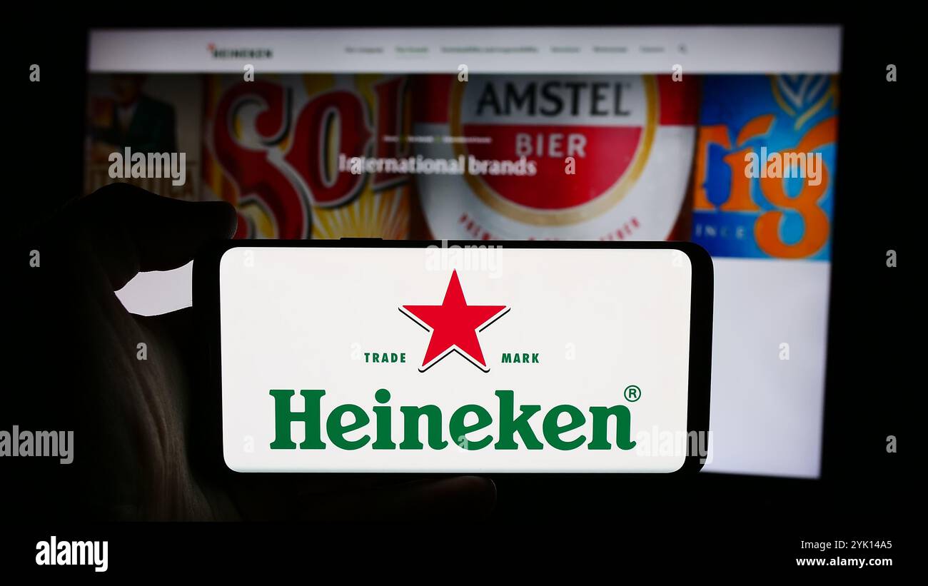 In questa immagine, una persona ha in mano un cellulare con il logo della società olandese Heineken N.V. davanti alla pagina Web aziendale. Foto Stock