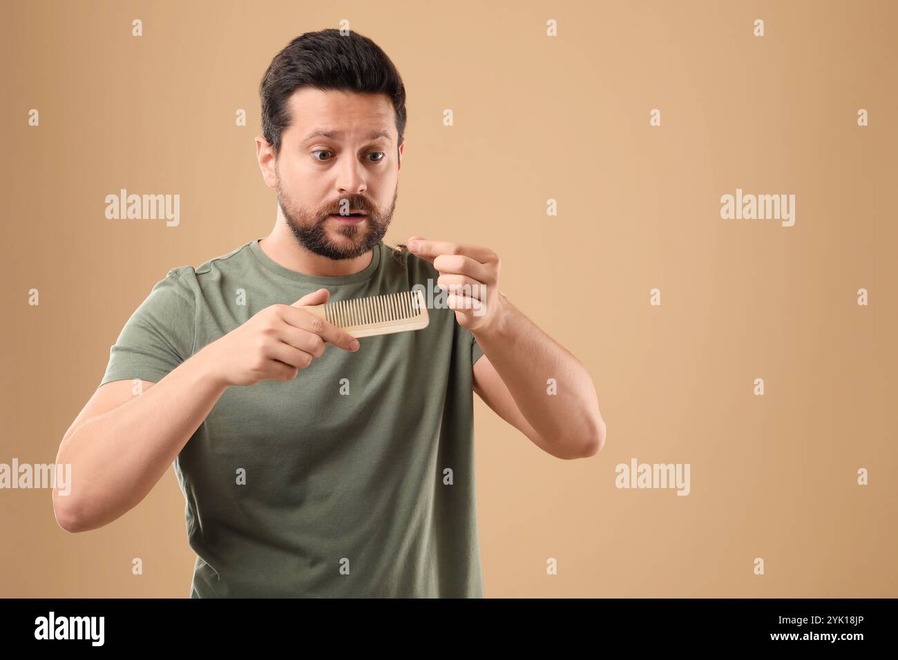 Uomo emotivo che prende i capelli persi dal pettine su sfondo beige, spazio per il testo. Problema di alopecia Foto Stock