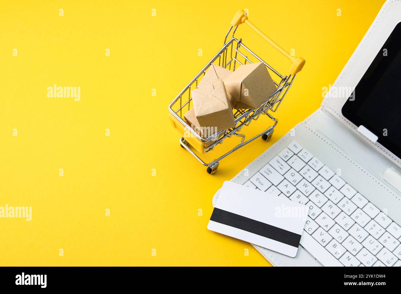 Carrello con scatole, carta di credito, tastiera bianca per computer portatile su sfondo giallo. Concetto di shopping online su Internet. Copia spazio Foto Stock