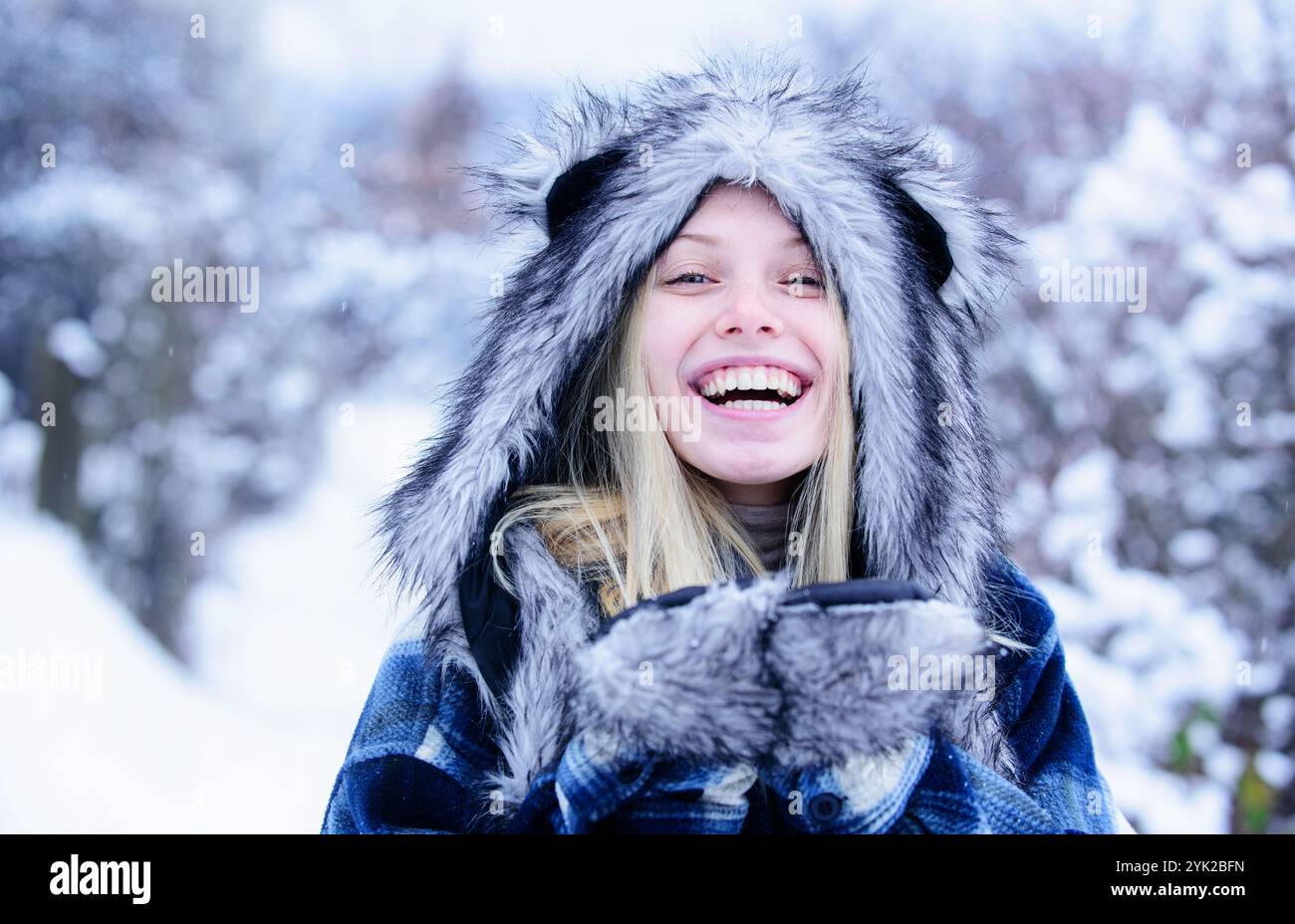 Ritratto ravvicinato di una ragazza sorridente con cappotto a scacchi, cappello di pelliccia e guanti che camminano nel parco invernale. Modella alla moda nella foresta invernale. Bella Chr Foto Stock