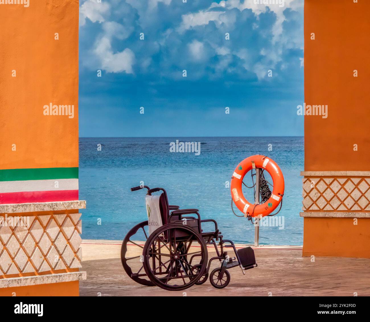 Sedia a rotelle e anello di salvataggio accanto all'oceano turchese in un resort di spiaggia tropicale, simboleggiando viaggi accessibili, mobilità, indipendenza e libertà Foto Stock