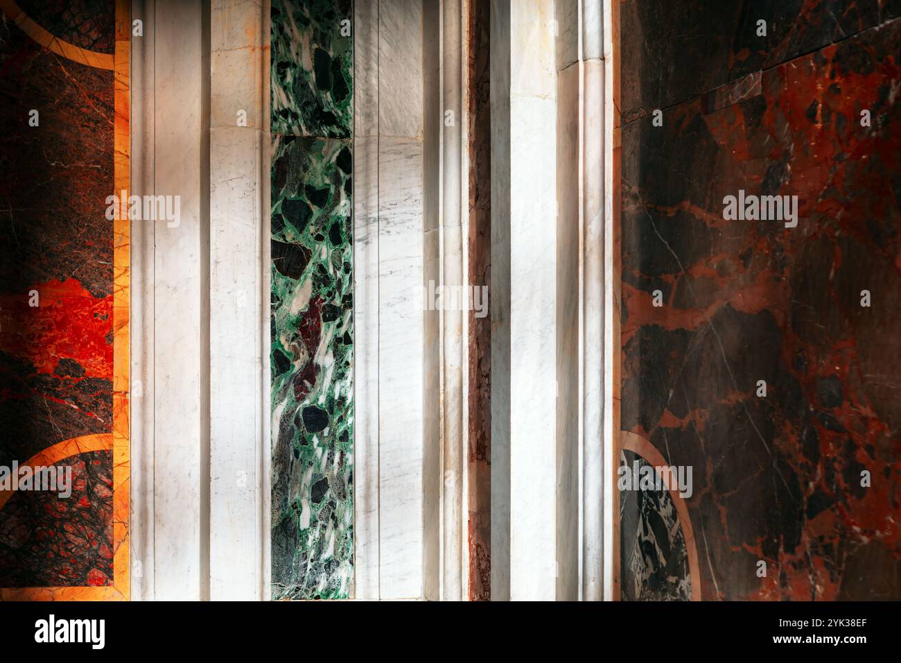 Sezione di una parete adornata con vari pannelli di marmo. I pannelli presentano colori e motivi diversi, tra cui tonalità di verde, bianco, rosso e nero, Foto Stock