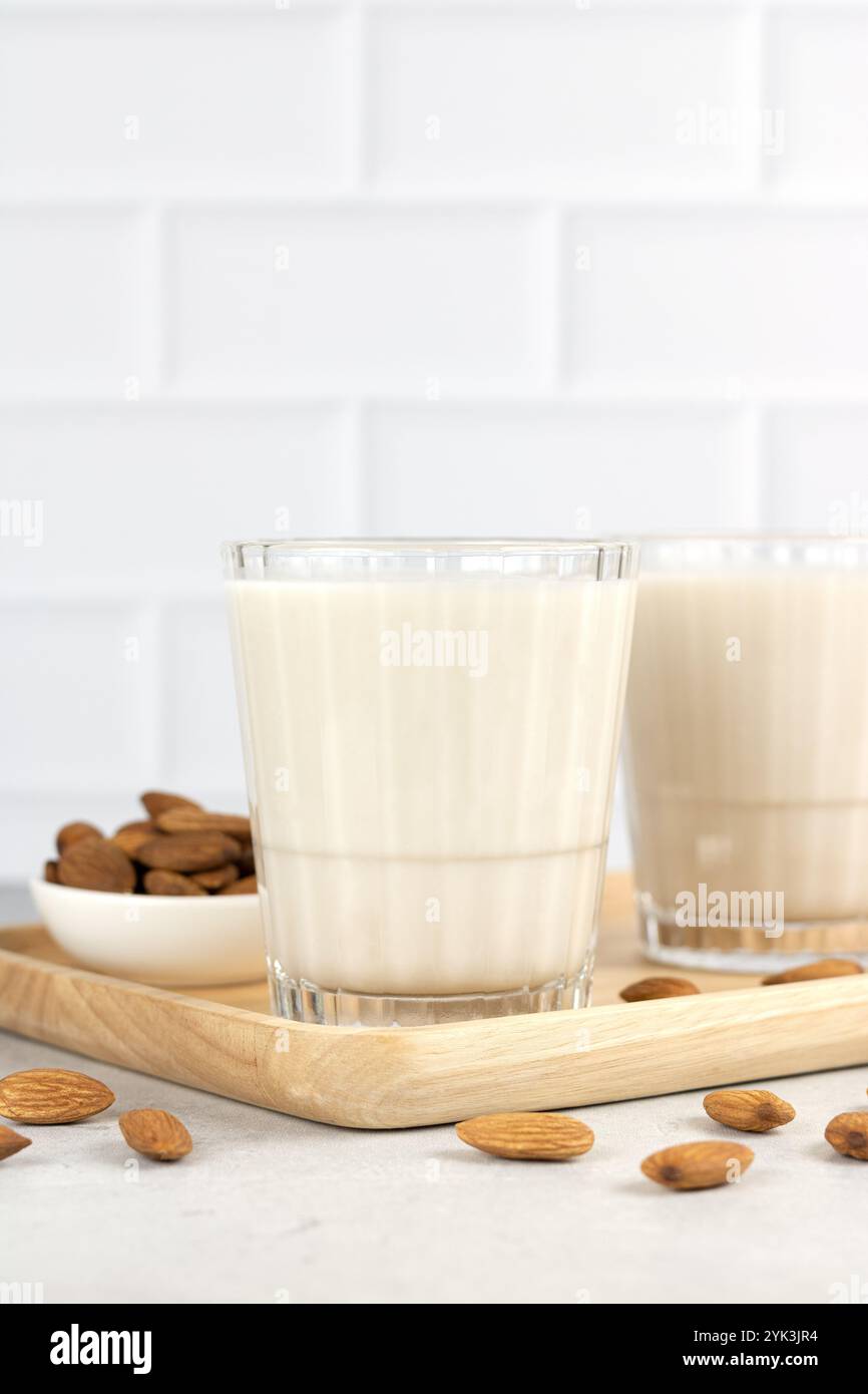 Latte di mandorle privo di lattosio in un bicchiere su un tavolo bianco e chicchi di mandorle. Copia spazio. Latte di noci biologico. Foto Stock
