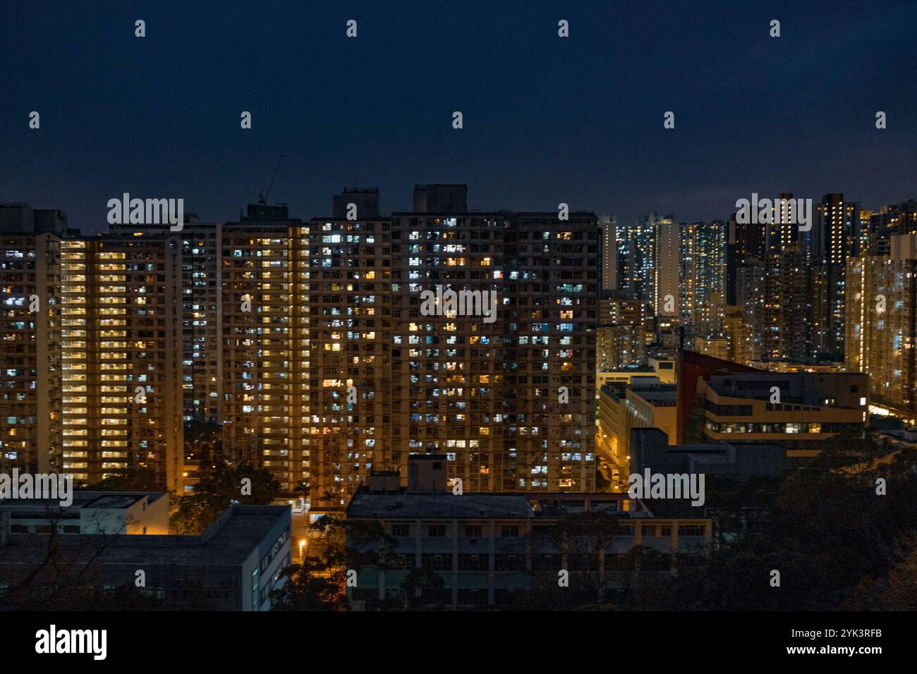 Numerose finestre illuminate illuminate illuminano di notte, rivelando la vita affollata delle famiglie che affrontano le sfide della vita urbana e i costi crescenti. Foto Stock