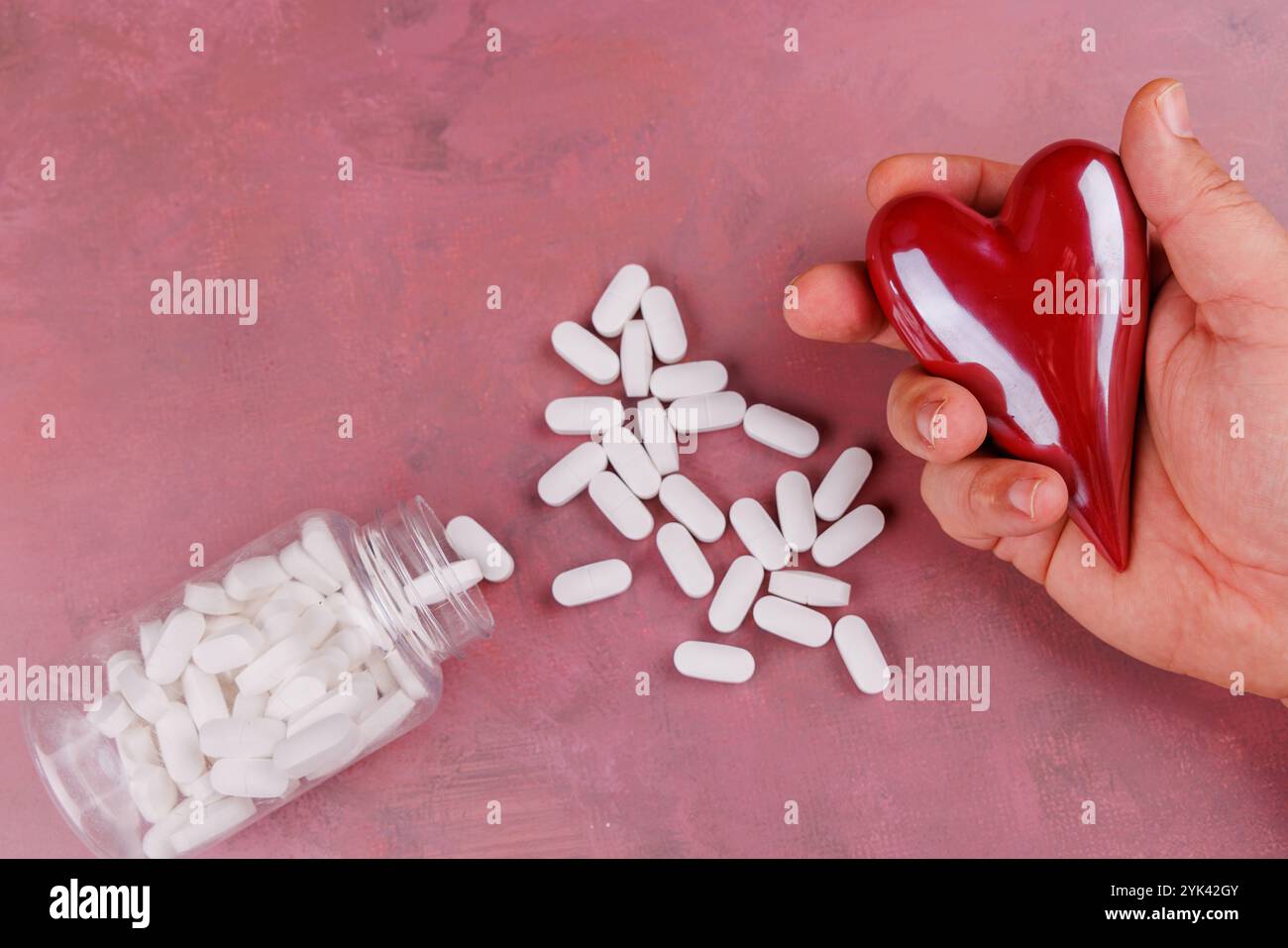 Foto ispirata a San Valentino con cuori in porcellana e pillole bianche su una superficie di cemento rosso, che simboleggiano le malattie cardiache in un sho dall'alto verso il basso Foto Stock