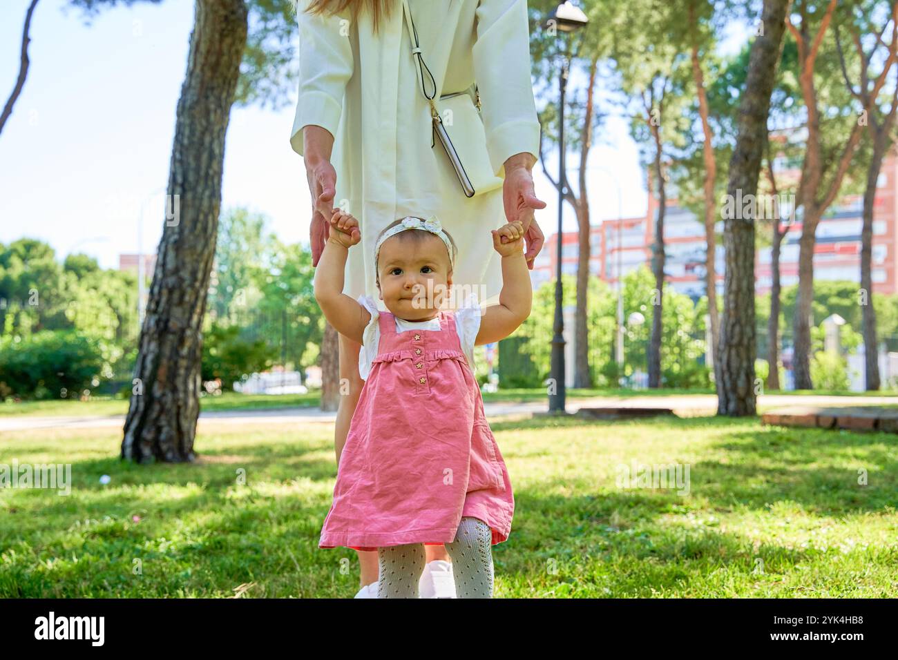 Una madre tiene il bambino per mano, aiutandolo a camminare nel parco. Il bambino sembra determinato e curioso, godendo del supporto e della guida Foto Stock