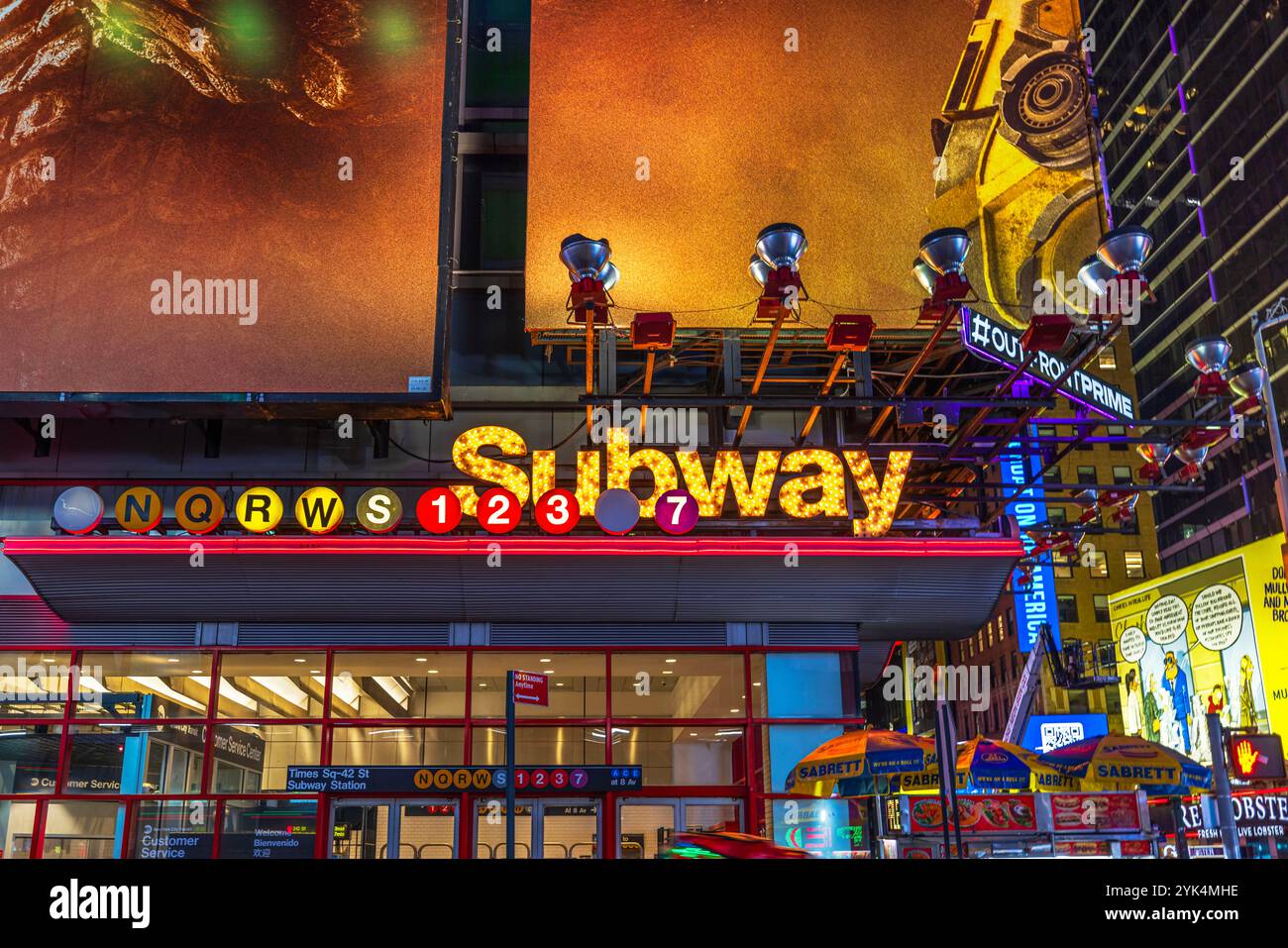 Luminoso cartello d'ingresso della metropolitana illuminato alla stazione di Times Square-42nd Street con cartelloni colorati e carrelli alimentari nelle vicinanze. New York. STATI UNITI. Foto Stock