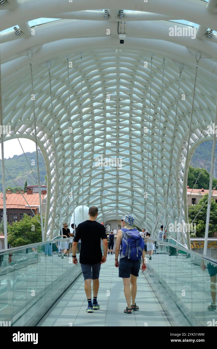 I pedoni attraversano il Ponte della Pace attraverso il fiume Kura, Tbilisi, Georgia Foto Stock