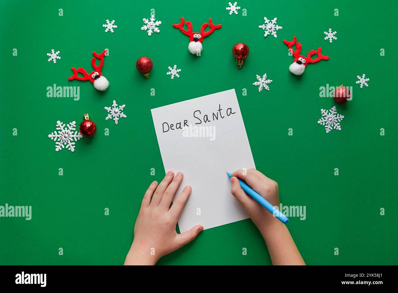 Decorazioni natalizie su sfondo verde. Il ragazzo tiene le mani in mano una matita per scrivere una lettera a Babbo Natale su un pezzo di carta artigianale. Vista dall'alto, flat la Foto Stock