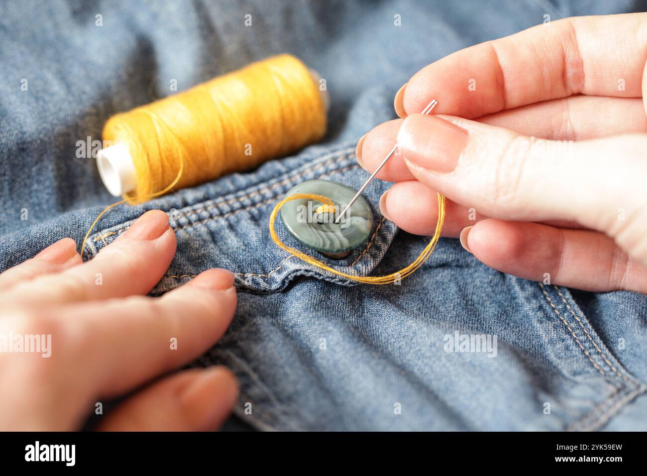 Donna che cucisce sul pulsante. Jeans con ago filettato per cucire. Primo piano. Stile di vita autentico. Fatto a mano Foto Stock