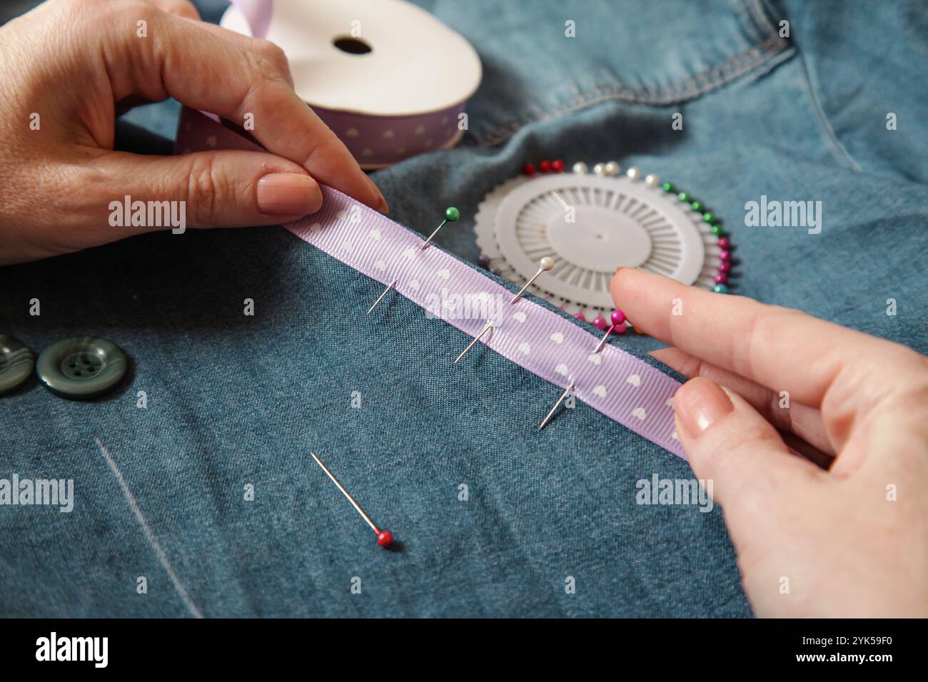 Donna che cucisce il nastro sul materiale dei jeans. Stile di vita autentico fatto a mano Foto Stock