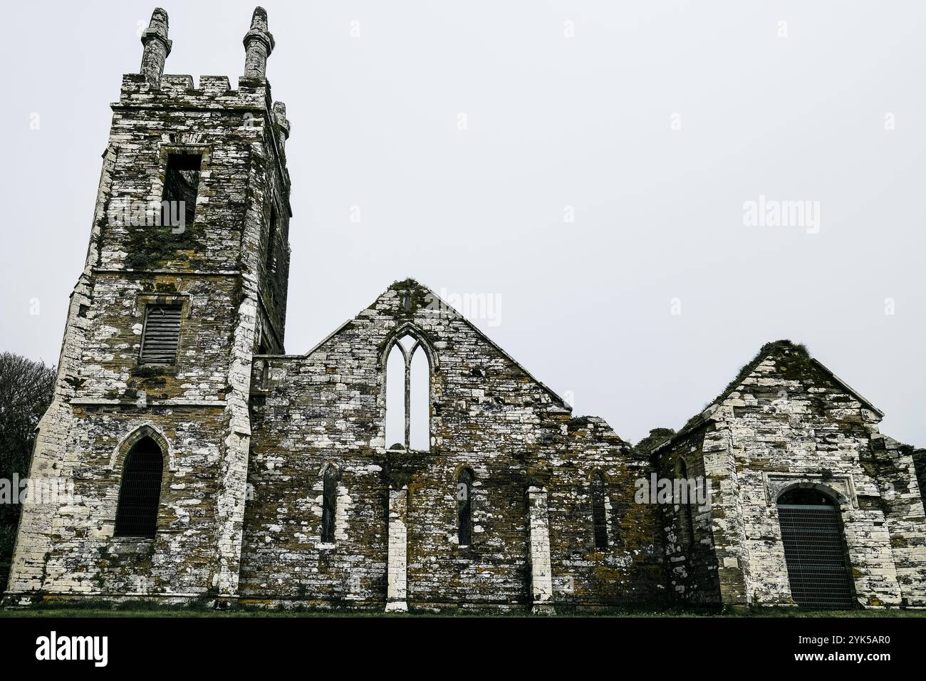 I resti di una chiesa in pietra si stagliano in modo prominente in un tranquillo paesaggio rurale, mostrando la sua architettura storica in mezzo a un'erba lussureggiante su un clo Foto Stock