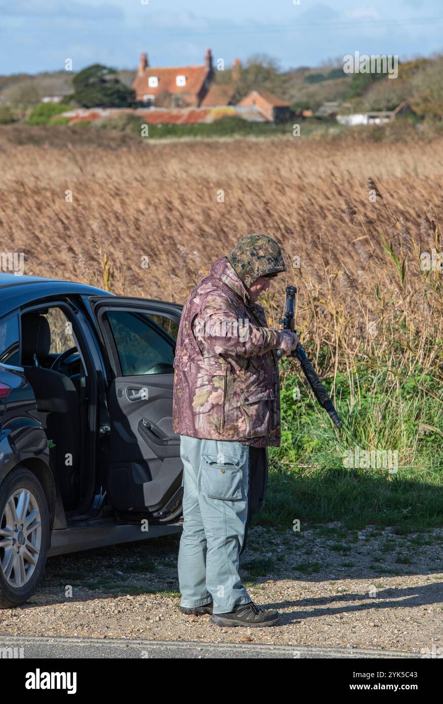 osservatore di uccelli o twitcher accanto all'auto vestito con abiti mimetici che preparano il suo telescopio, il treppiede e l'attrezzatura da fotocamera per una giornata in campagna per fare birdwatching. Foto Stock