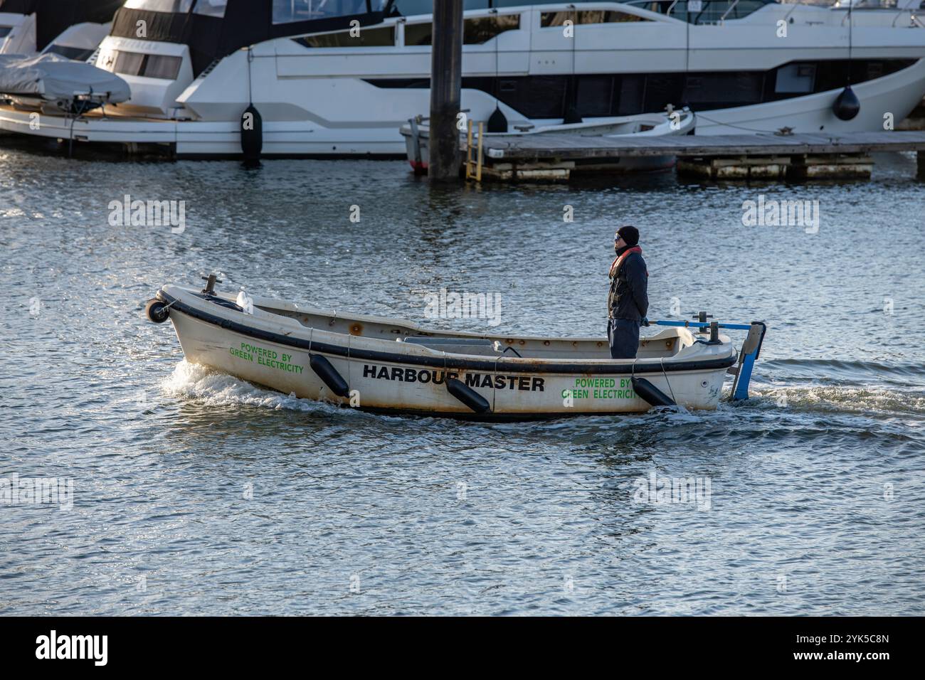 Porto turistico di Lymington e porto fluviale che guidano un piccolo varo o una barca con timone attraverso gli ormeggi e i pontili per manutenzione e costi di ormeggio Foto Stock