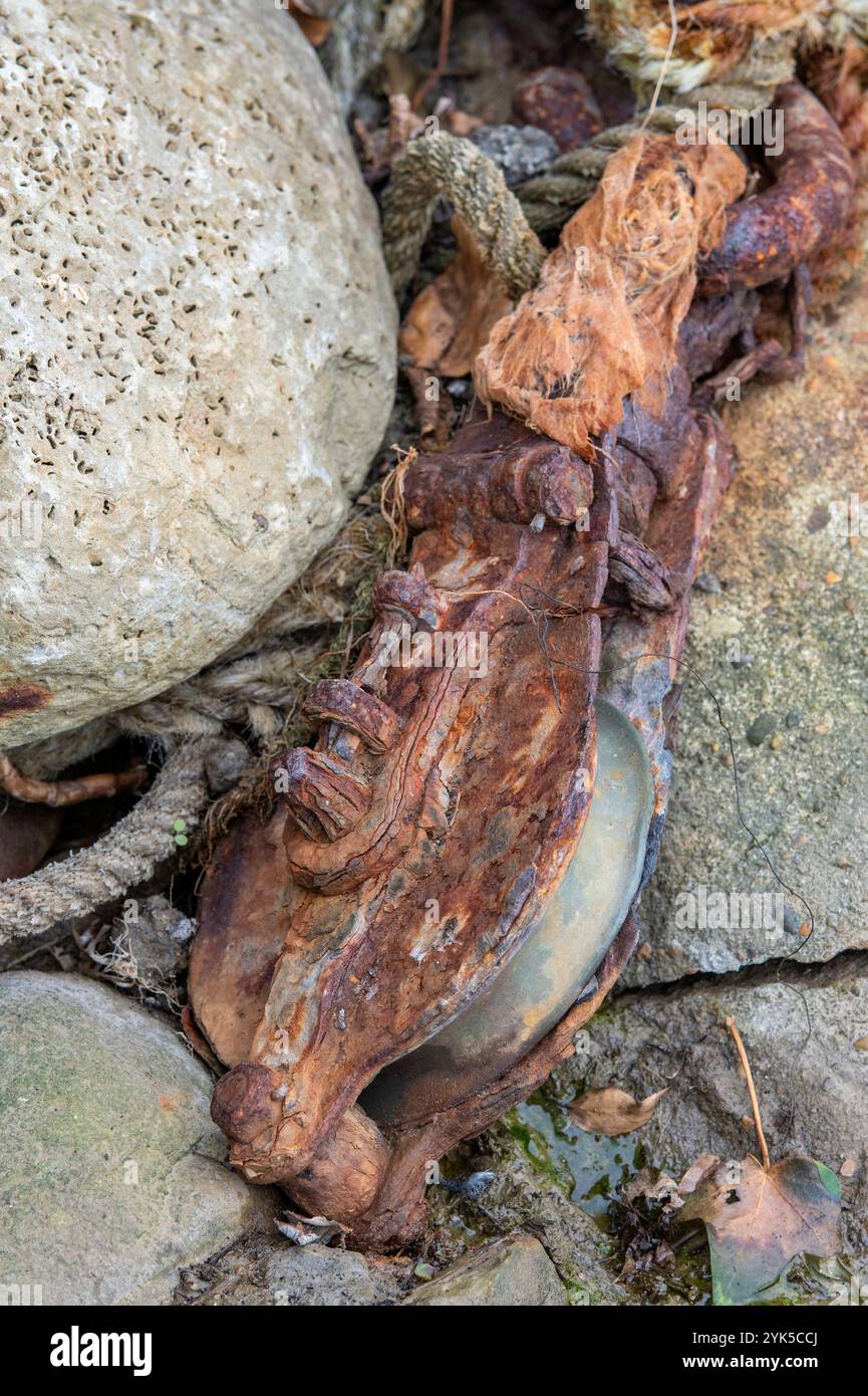 primo piano di vecchi blocchi di carrucole arrugginiti e corrosi e affronta abbandonati su una costa rocciosa, le navi si bloccano a sinistra per marcire su una spiaggia rocciosa. Foto Stock