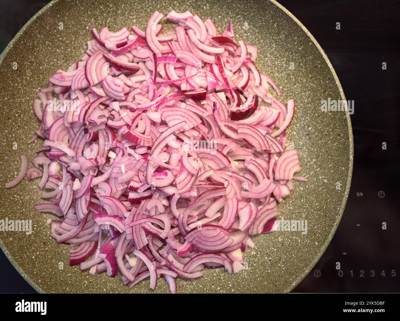 Le cipolle rosse a fette stanno cucinando in una padella a fuoco medio, rilasciando il loro aroma saporito mentre vengono preparate per un piatto. Foto Stock