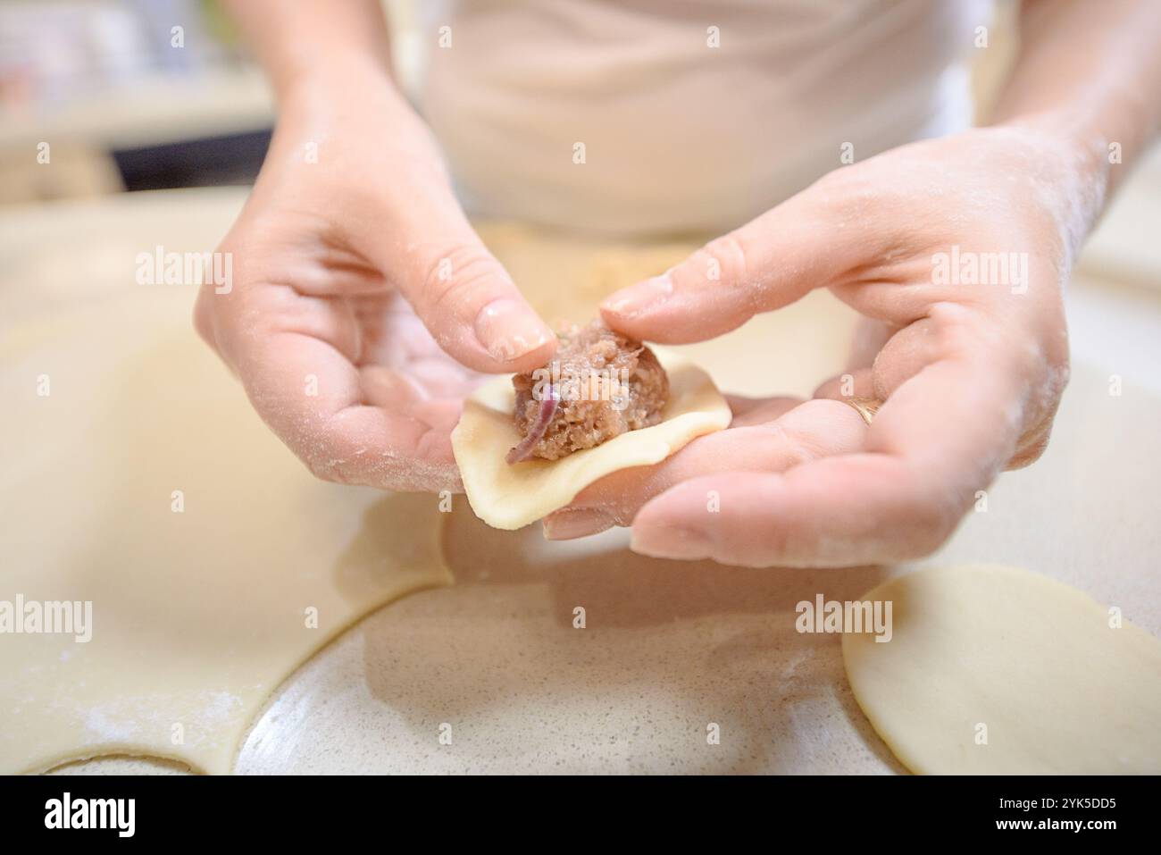 Due mani preparano sapientemente un gnocco, posizionando un ripieno di carne su un impasto rotondo in una cucina calda. Foto Stock