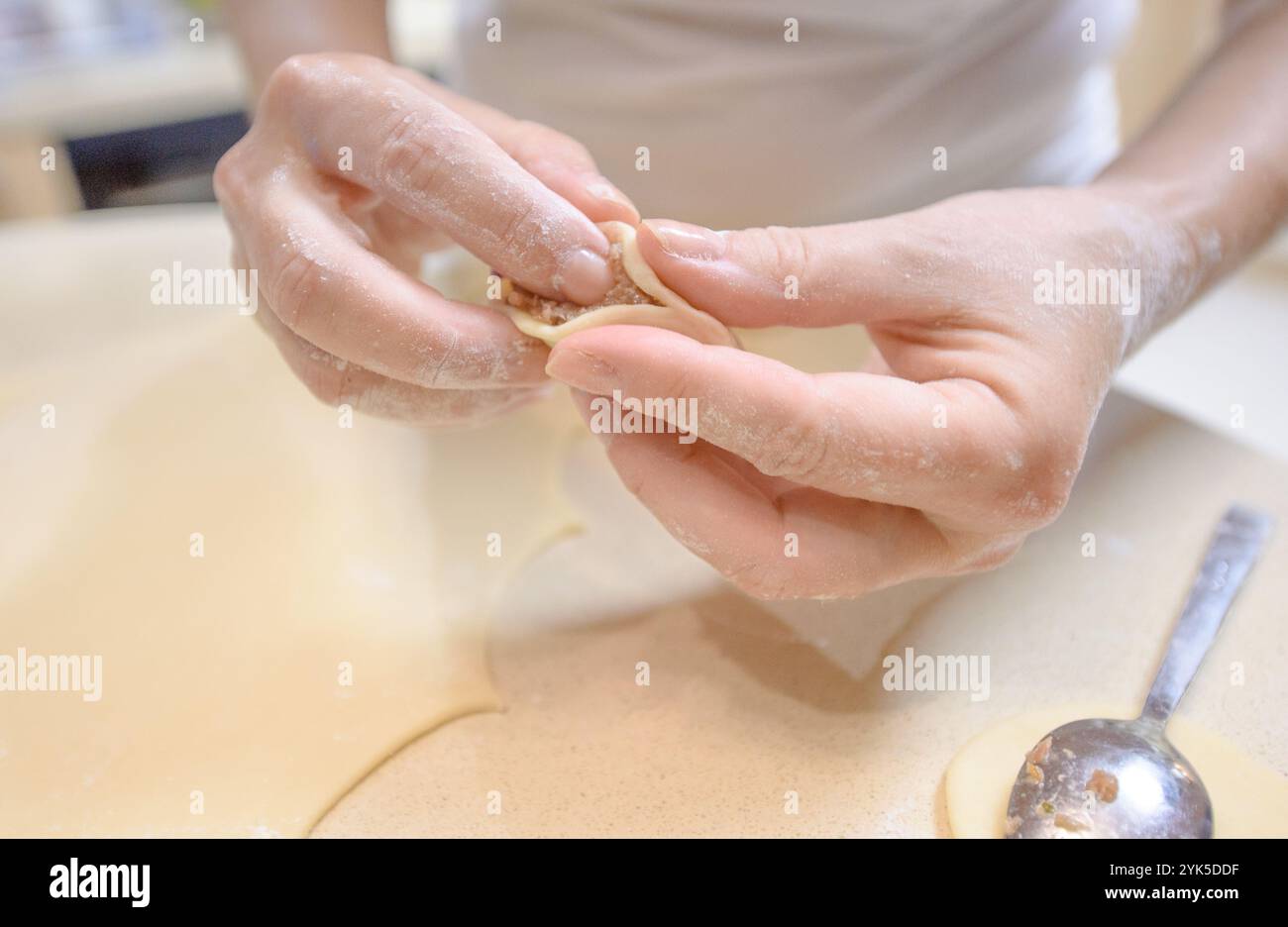 Mani esperte modellano sapientemente i gnocchi tradizionali con ripieno di carne, circondati da un ripiano spolverato di farina in una calda cucina. Foto Stock