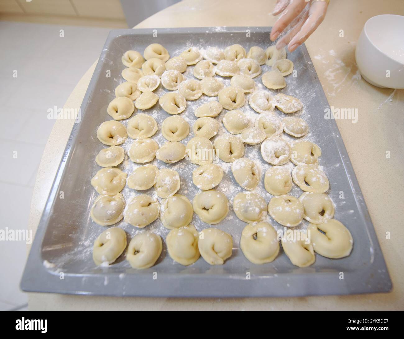 Una persona prepara gnocchi tradizionali modellando l'impasto riempito con ingredienti su un vassoio da forno in una cucina ben illuminata. Foto Stock