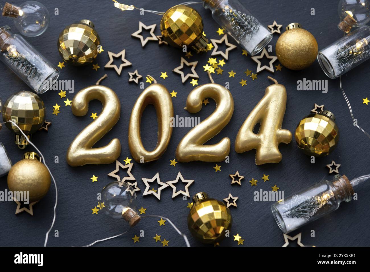 Le figure dorate 2024 fatte di candele su uno sfondo di ardesia di pietra nera sono decorate con un decor festoso di stelle, paillettes, rami di abete, palle e Foto Stock
