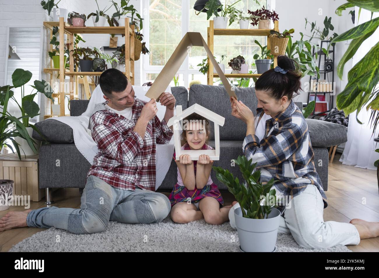 La famiglia tradizionale con bambino si sta godendo una nuova casa, seduto sul divano e tenendo il tetto. Mutuo, assicurazione e protezione, comprarmi e traslocare io Foto Stock