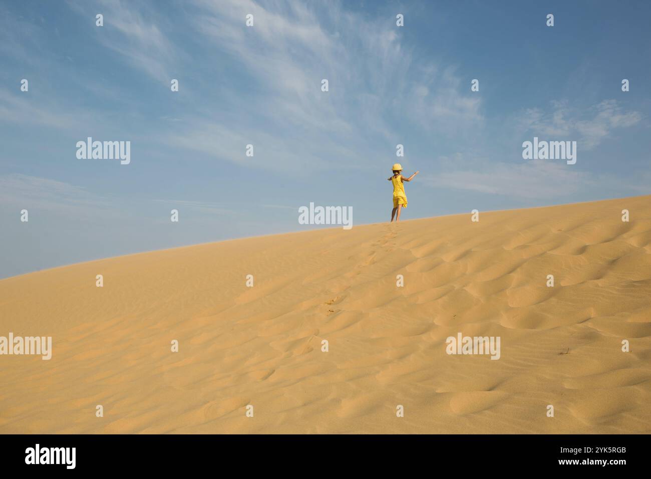 Una ragazza turistica in abito giallo corre lungo una duna sabbiosa nel deserto. Viaggio, attrazioni turistiche di Dagestan, Sarykum duna Foto Stock