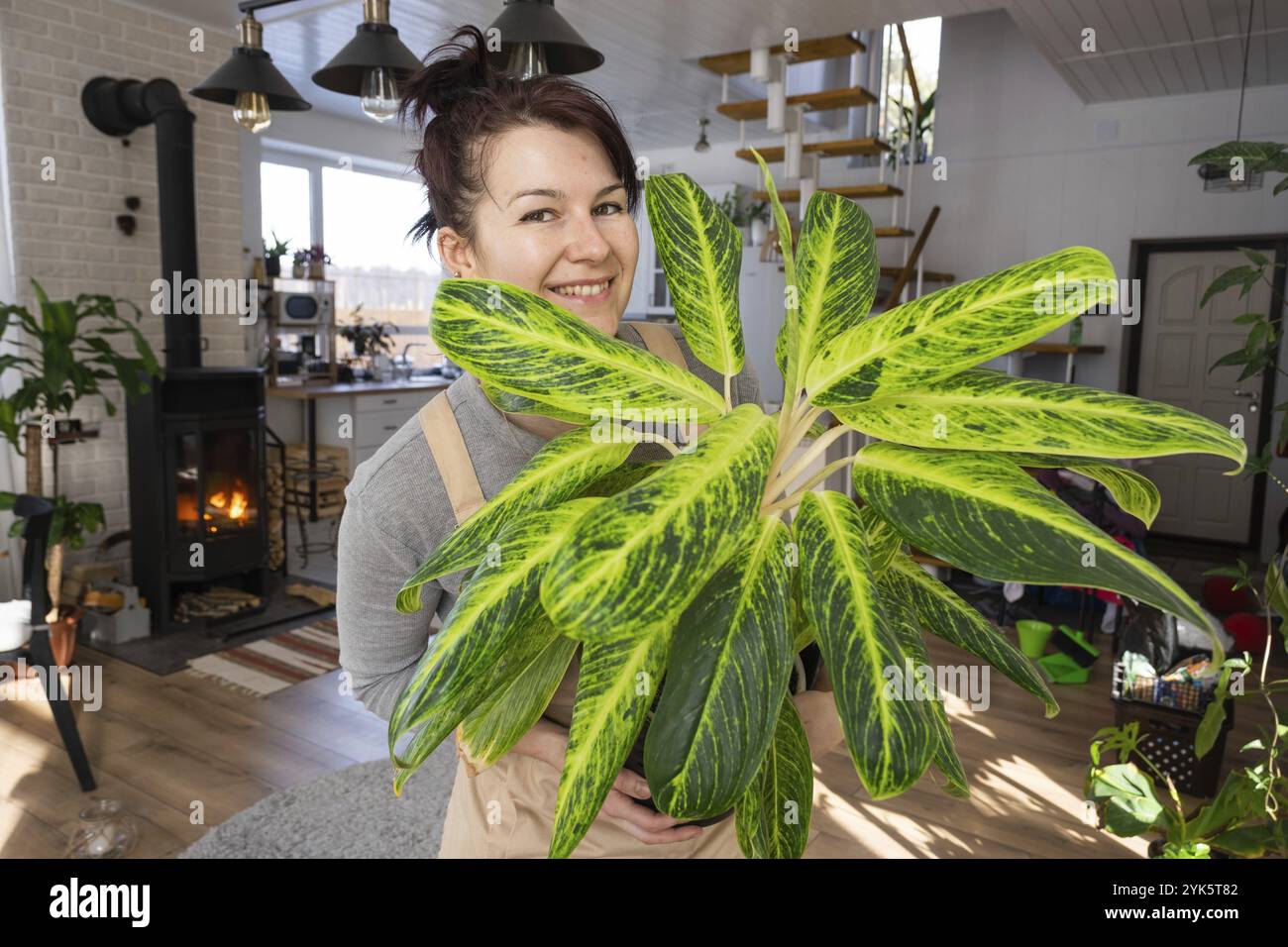 Una donna felice in una casa verde con una pianta in vaso nelle sue mani sorride, si prende cura di un fiore. L'interno di una casa accogliente eco-friendly, un camino Foto Stock