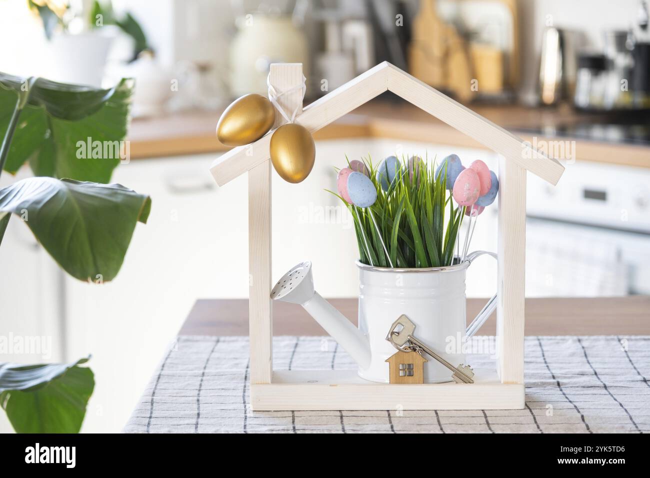 Chiave e piccola casa di casa accogliente con arredamento pasquale con uova colorate sul tavolo della cucina. Costruzione, progettazione, progetto, trasferimento in nuova casa, mutuo, insur Foto Stock