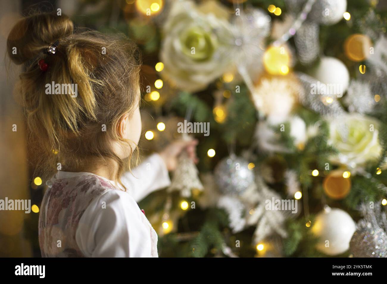 Una bambina raggiunge per un giocattolo dell'albero di Natale con la sua mano. Decorazioni natalizie, in attesa di una vacanza e di un miracolo. Anno nuovo. Bianco, rosa e blu dec Foto Stock