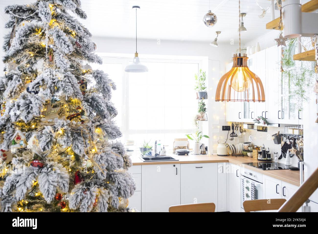 Decorazioni natalizie natalizie in cucina bianca, interni rustici moderni con un albero di Natale innevato e luci delle fate. Capodanno, atmosfera natalizia, casa accogliente. TH Foto Stock