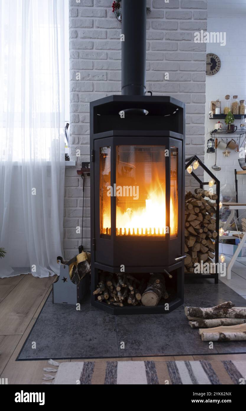 Stufa nera, camino all'interno della casa in stile loft. Riscaldamento ecologico alternativo, camera calda e accogliente a casa, legna da ardere Foto Stock
