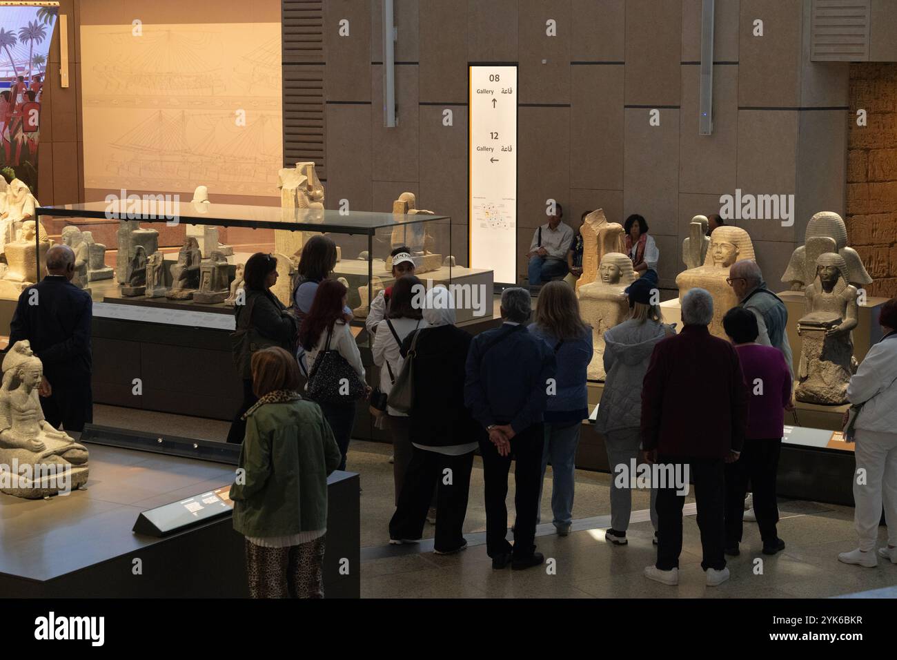 I visitatori nella galleria 7 del Grand Egyptian Museum ascoltano attentamente la loro guida raccontando loro della società nel nuovo Regno (1550-1070 a.C.). Foto Stock