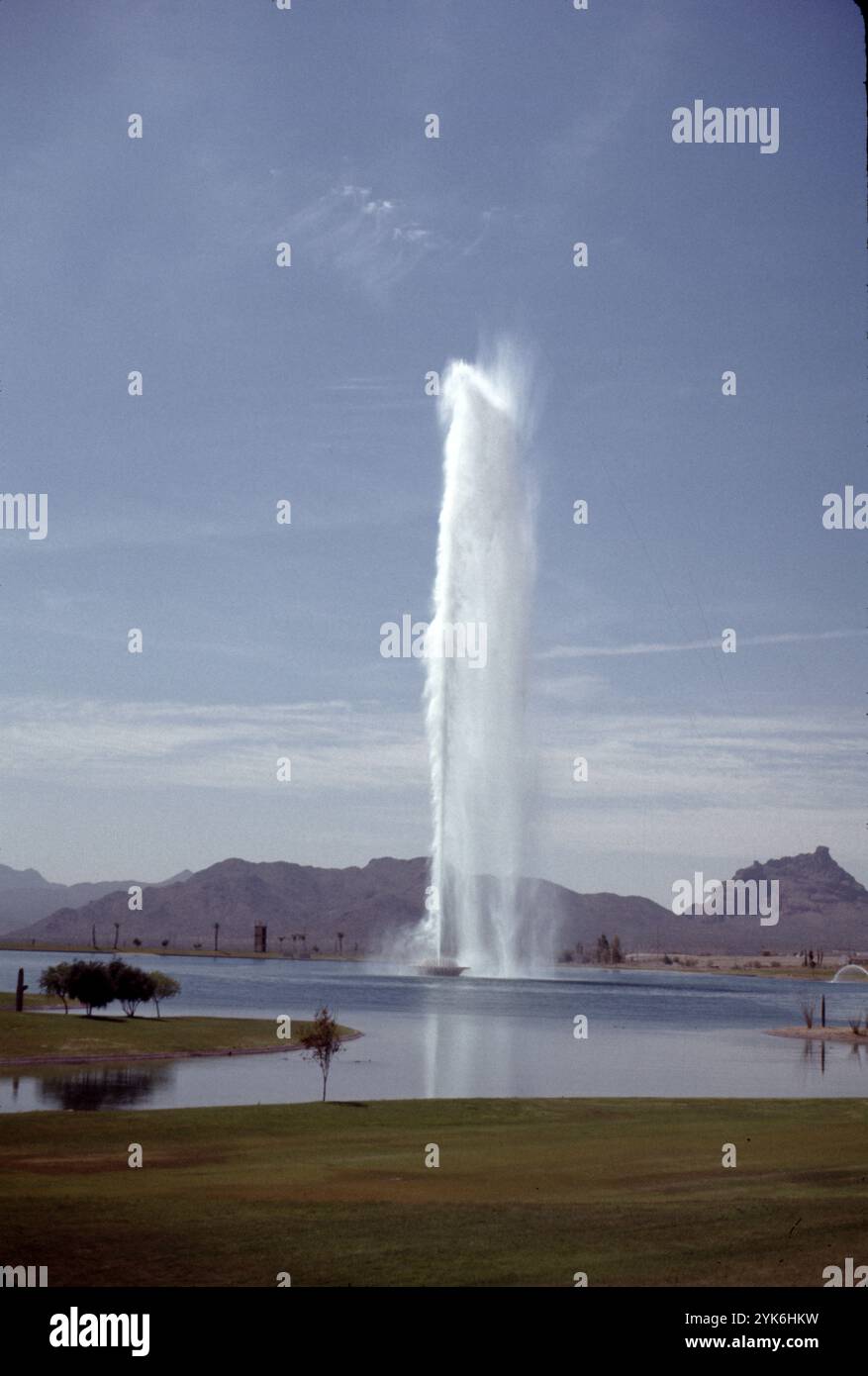 Fountain Hills, Arizona. U.S.A. 1975. Fountain Hills ha la quarta fontana più alta del mondo e la seconda più alta degli Stati Uniti. Fu costruito nel 1970 a Zürich da Robert P. McCulloch. l'anno prima. La fontana spruzza acqua per circa 15 minuti ogni ora tra le 9:00 e le 21:00. Il pennacchio sorge da una scultura di giglio d'acqua in cemento al centro di un grande lago artificiale. La fontana, azionata da tre pompe a turbina da 600 CV (450 kW), spruzza acqua a una velocità di 7.000 galloni USA (26.000 L; 5.800 imp gal) al minuto attraverso un ugello da 18 pollici (460 mm). Foto Stock