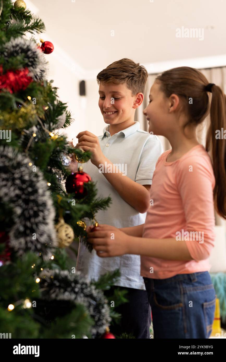 Ragazzo e ragazza caucasici decorano un albero di Natale a casa Foto Stock