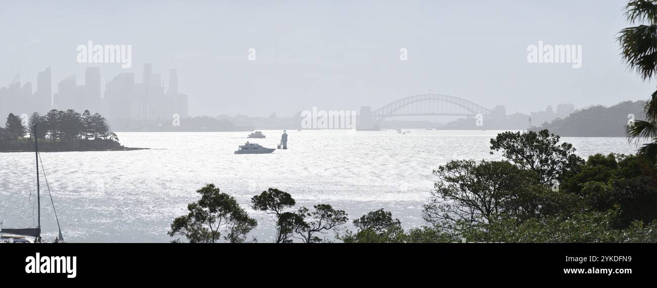 Sydney, Australia, panorama del Sydney Harbour Bridge e dell'Opera House sotto una nebbia leggera, lo skyline del CBD con una silhouette spettrale e la luce del sole sull'acqua Foto Stock