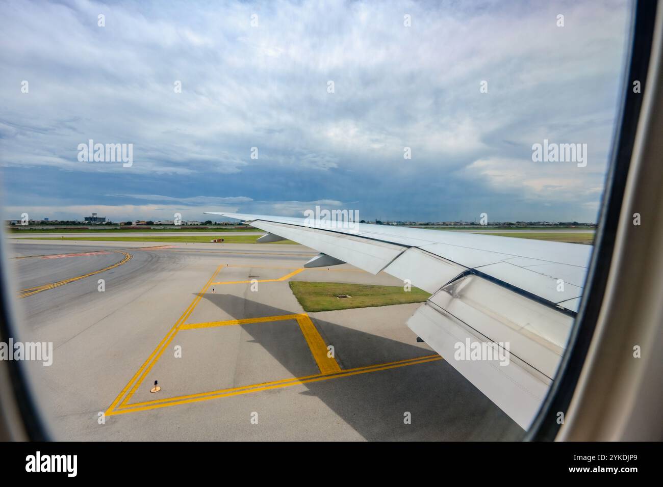 Attraverso la finestra dell'aereo, l'Aeroporto Internazionale di Suvarnabhumi viene in vista, insieme alle ampie ali dell'aereo, nel mezzo del trambusto di mezzogiorno Foto Stock