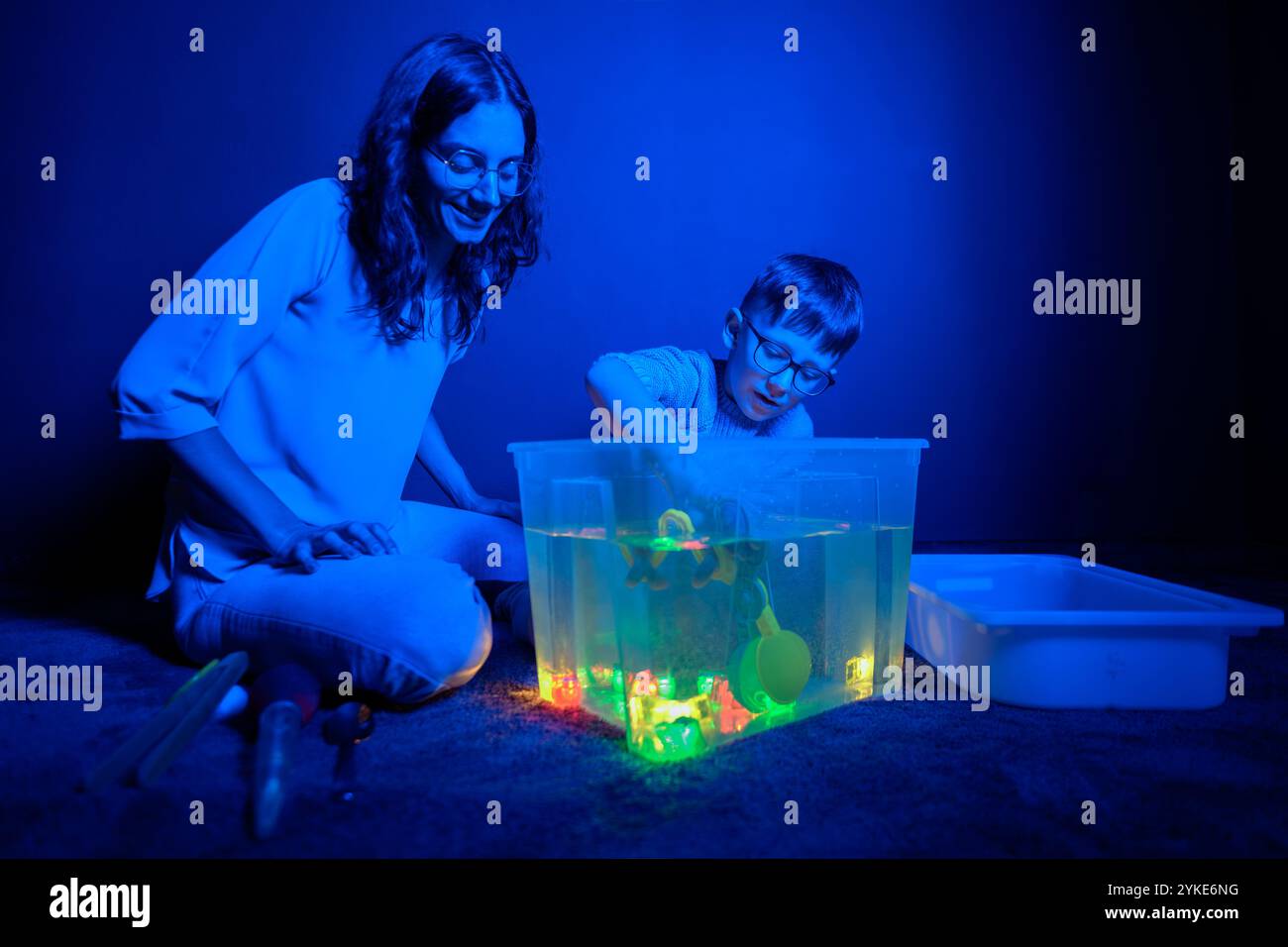 Bambino e terapista in camera stimolante sensoriale, Black snoezelen. Bambino autistico che gioca con il terapista durante la sessione di terapia occupazionale. Foto Stock