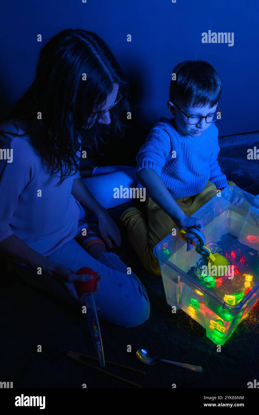 Bambino e terapista in camera stimolante sensoriale, Black snoezelen. Bambino autistico che gioca con il terapista durante la sessione di terapia occupazionale. Foto Stock